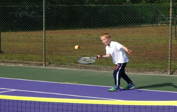 Boy playing tennis in blue tracksuit bottoms and white polo shirt 