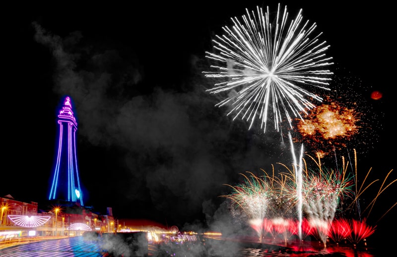 Fireworks over beach and brightly lit tower