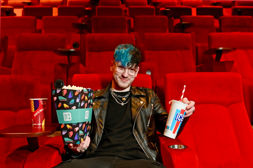 Person sat in cinema holding popcorn and drink.