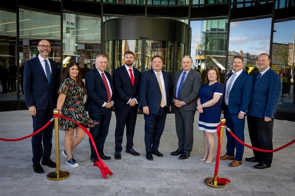 A series of people stood in front of the new office cutting a ribbon