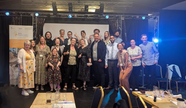 Project SEARCH interns and team members celebrate graduation together in front of a large screen.
