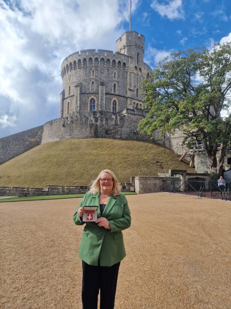 Cllr Lynn Williams smiles whilst standing in front of Windsor Castle holding her MBE award