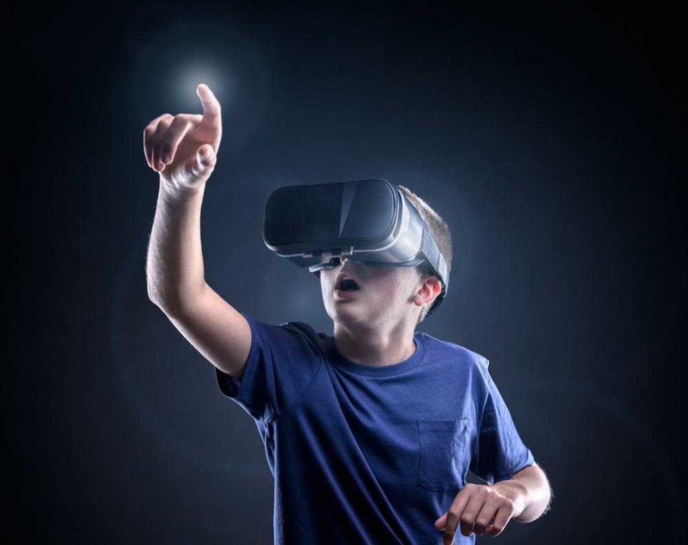 Teenage male wearing a virtual reality headset pointing to tap something in front of him
