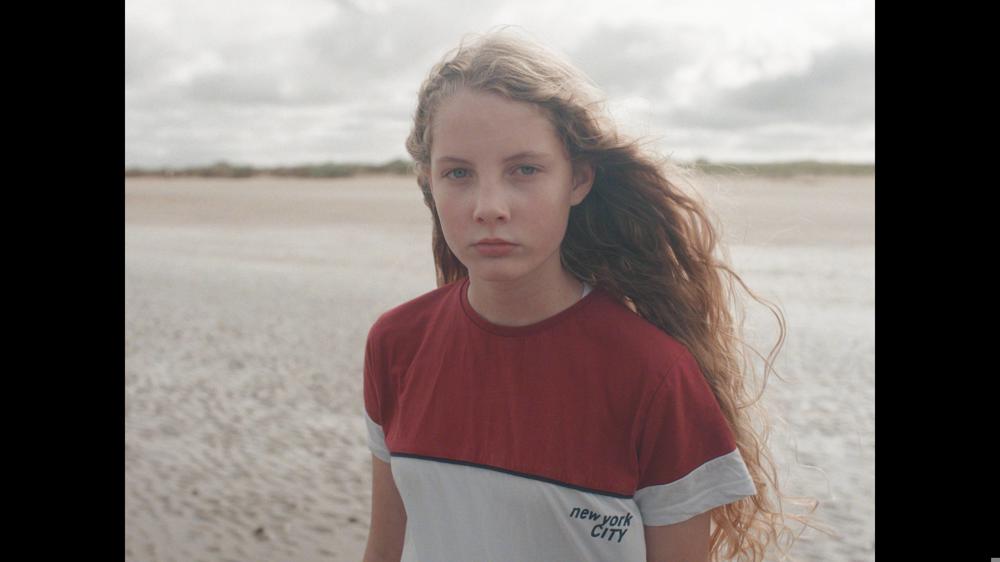Young girl on beach looking sad at the camera