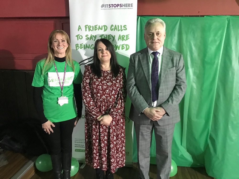 Two women and a man stood in front of a banner