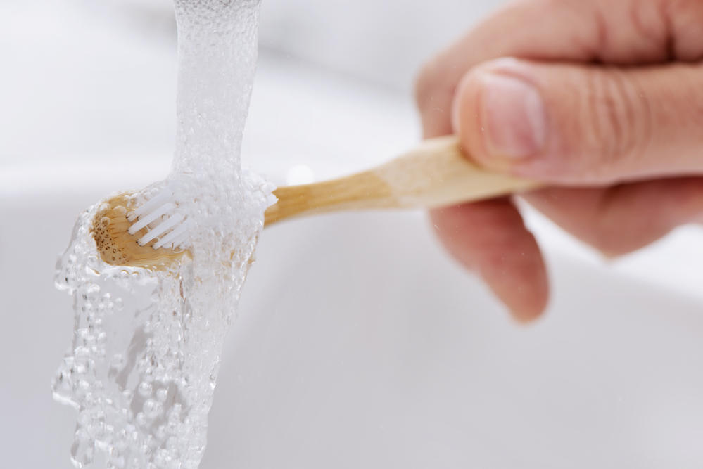 A wooden toothbrush being cleaned under running water