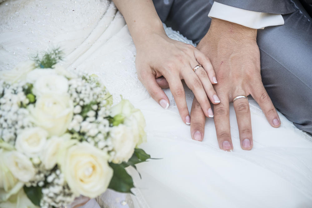 Bride and groom hands with wedding rings and flower bouquet