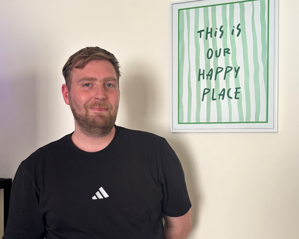 A man standing proudly in his new home - a sign reads 'This is our happy place'