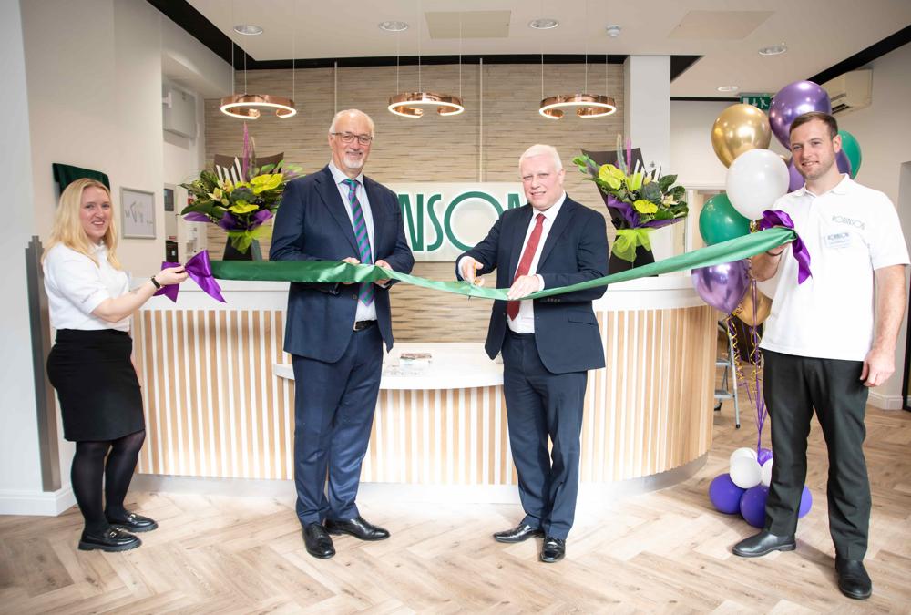 Four people smile at the camera whilst holding a green ribbon in front of a reception desk