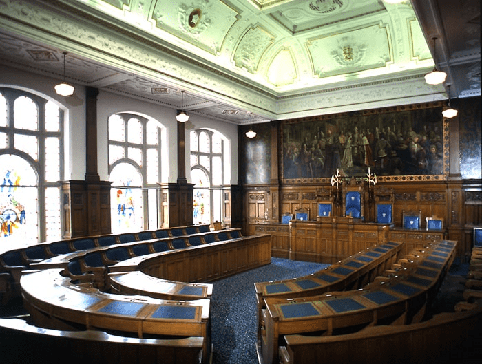 Ornate oak desks in semi-circle looking towards central desk with large backed chairs.