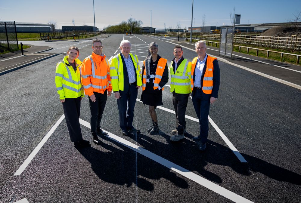 Six people wearing high-vis vests stood in the centre of a newly completed road. 