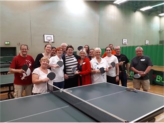Group of people stood round a tablet tennis table all holding bats