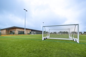 A photo of a 3G pitch with goalposts and a pavilion in the background