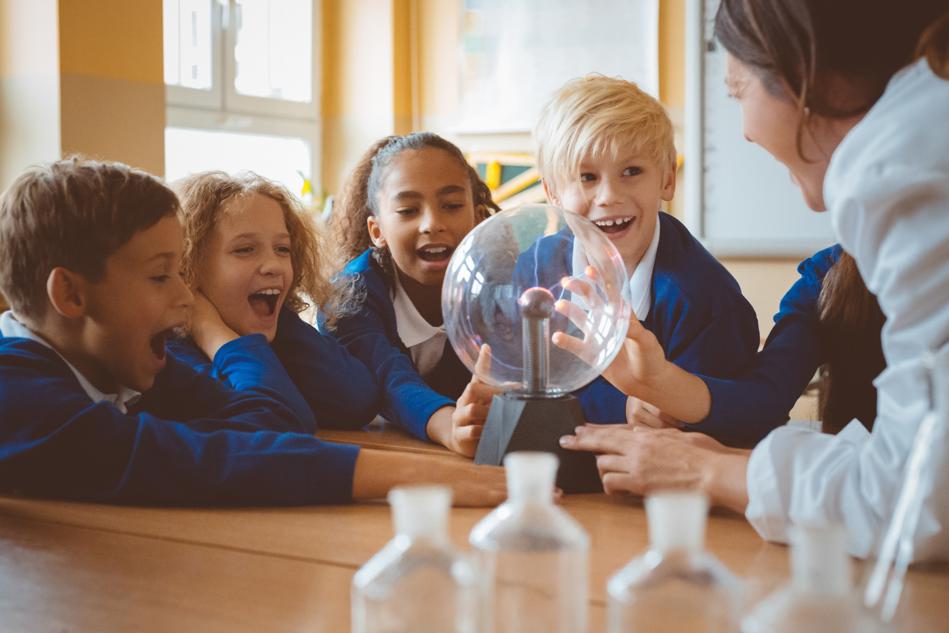 Smiling children in group around science equipment with teacher.