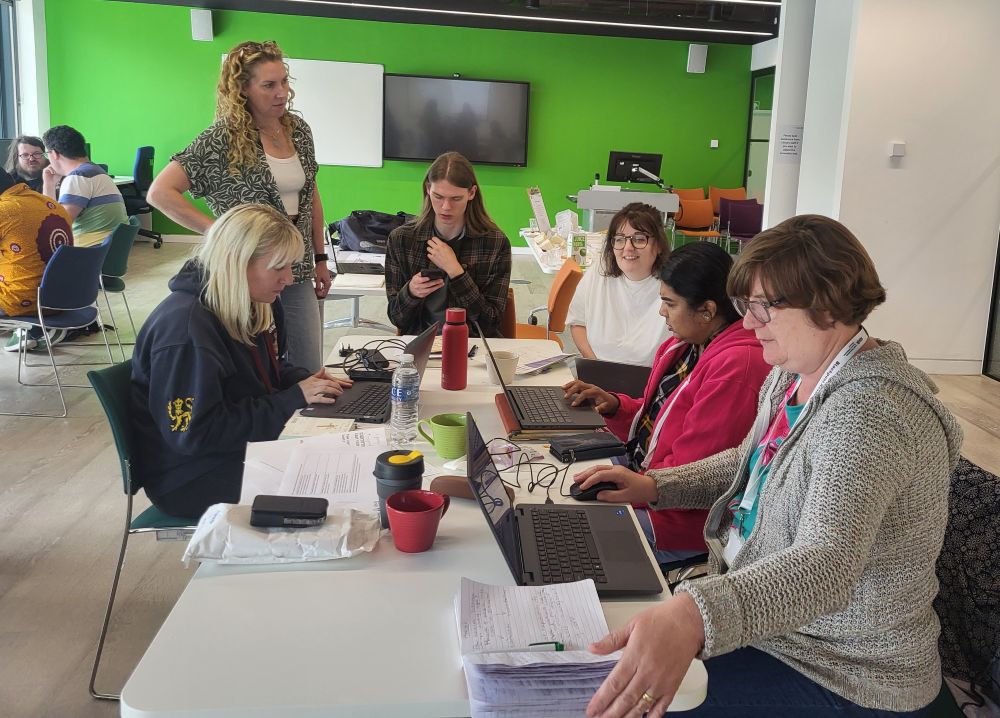 Group of people on a table working together, with a lady assisting.