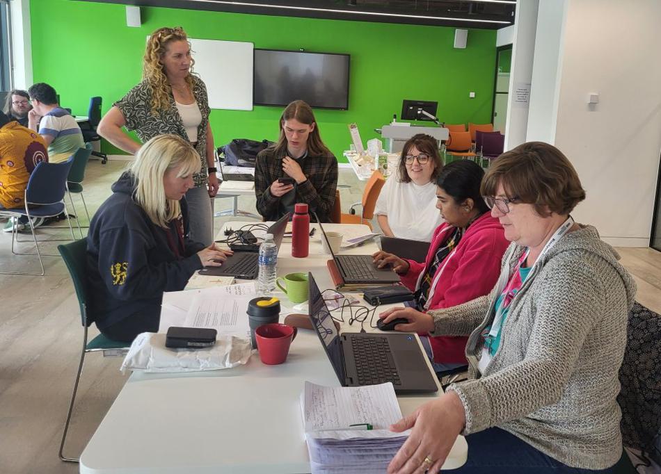 Group of people on a table working together, with a lady assisting.