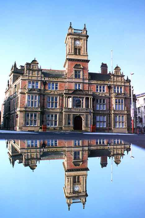 Victorian brick and stone building with clock tower with reflection in car roof.