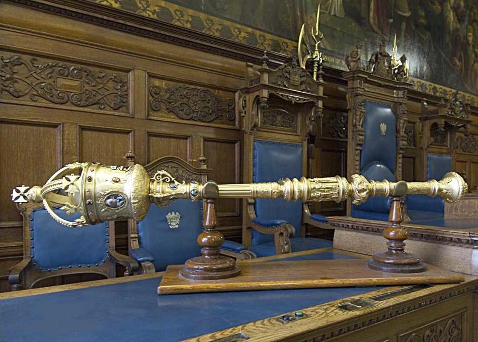 Golden mace with crown sitting on oak stand.