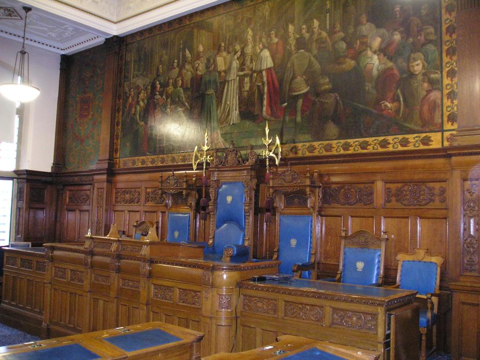 Oak paneled desk with ornate blue chairs and large oil painting behind.