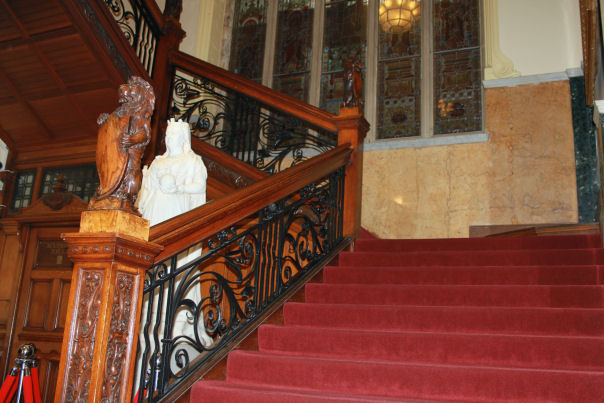 Red carpeted ornate staircase with statue in the background.