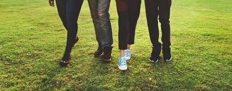 Four people's legs walking on green grass