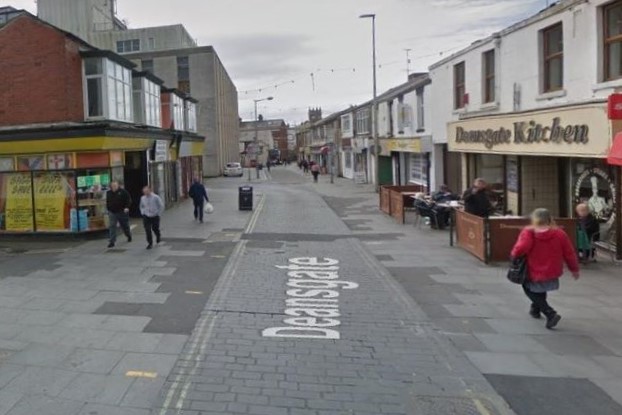 old paved road with broken footpaths with shops on both sides