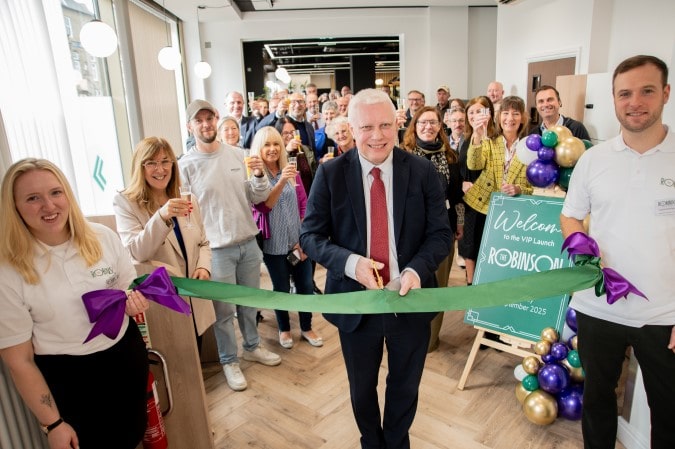 Man cutting ribbon surrounded by group of people.