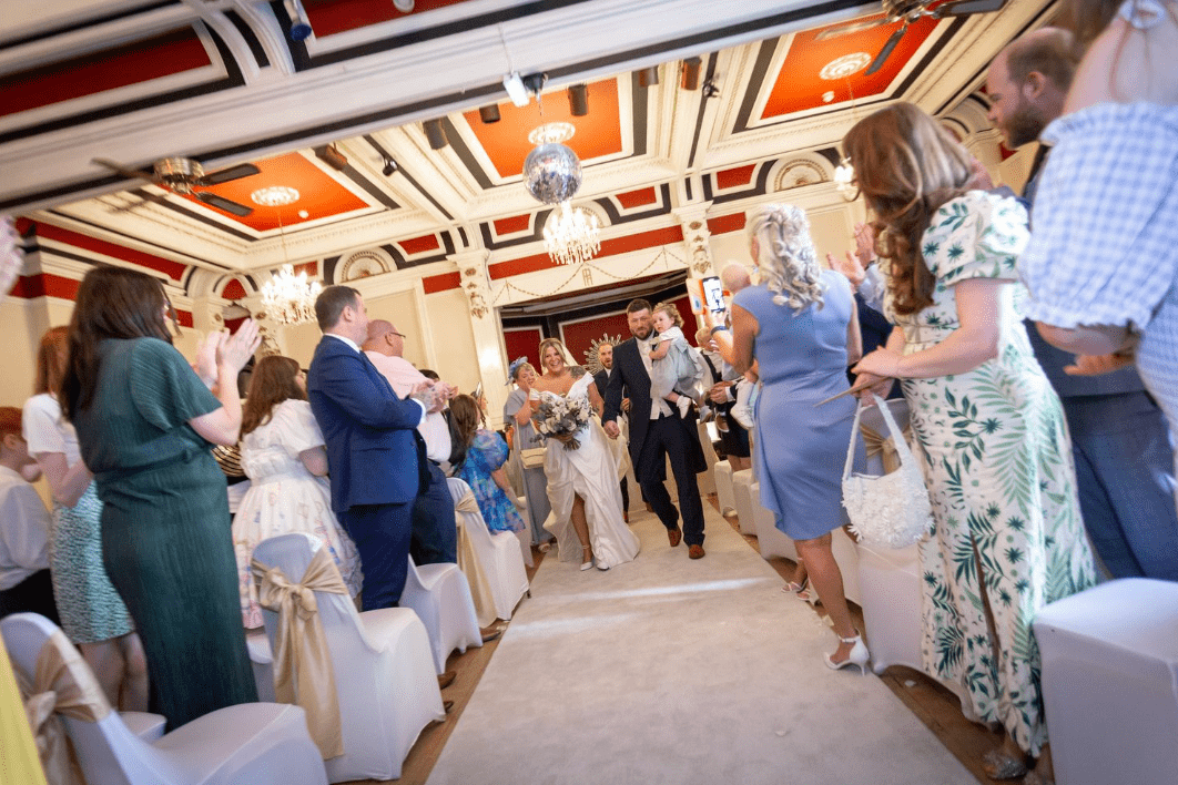 Bride and groom holding a child walking surrounded by people clapping