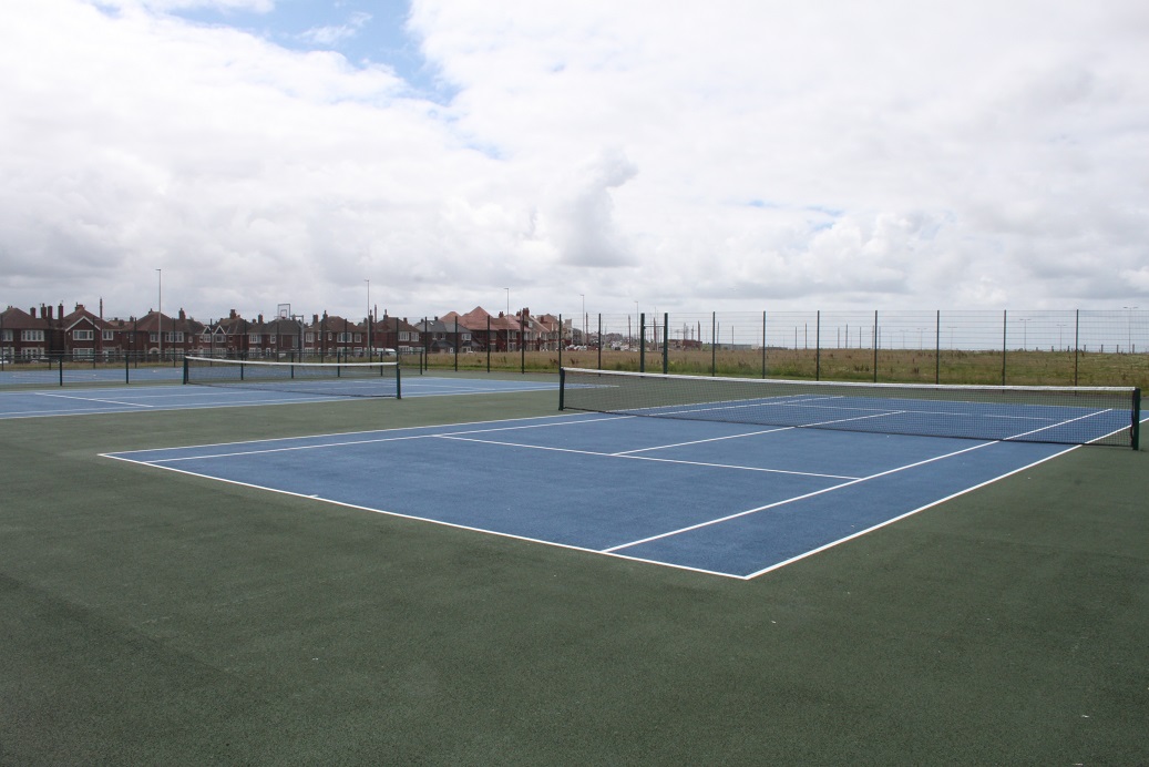 Two blue tennis courts in a park on a summer day