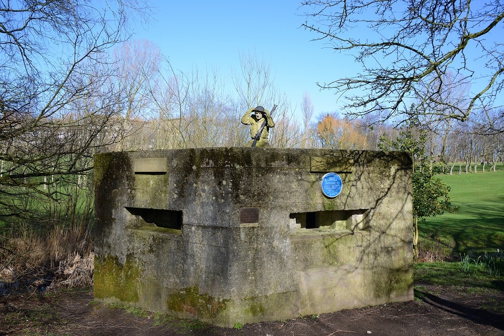 World War 2 pill box with statue of soldier kneeling on top.