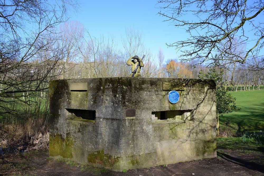 World War 2 pill box with statue of soldier kneeling on top.