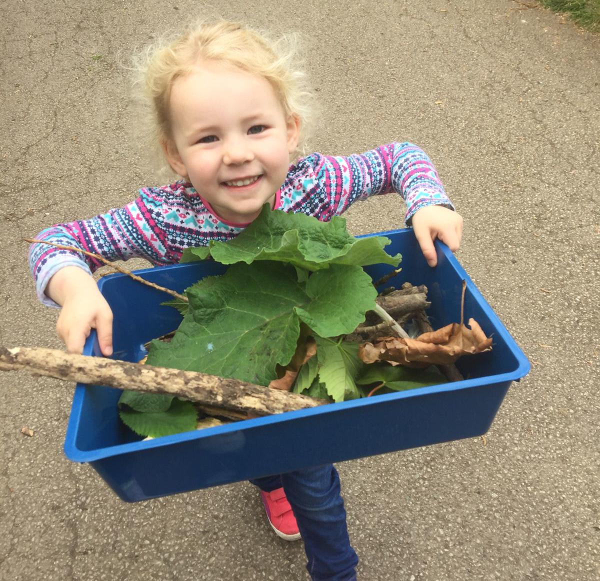Child holding a box filled with sticks and leaves
