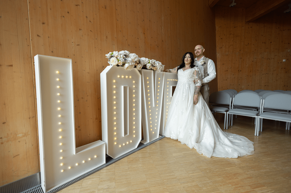Bride and groom stood in front of illuminated love sign