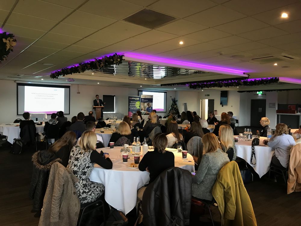 Blackpool Researching Together Annual Learning Event image showing groups of participants seated at tables while the presenter addresses the room.